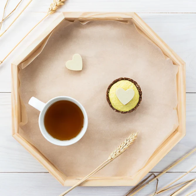 A wooden tray with a cup of tea and a heart shaped cupcake.