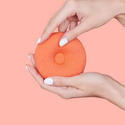 Hands holding a round, orange warm compress eye cup of a steam eye mask.