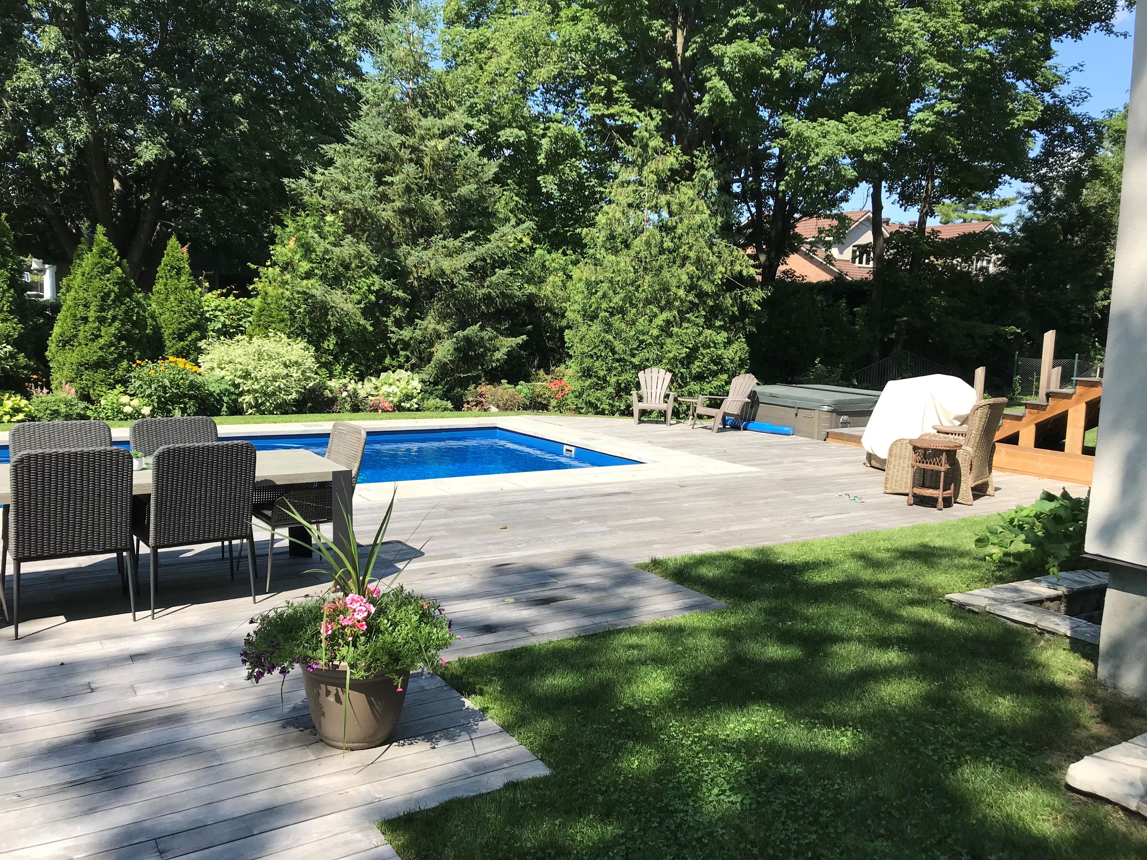 pool side deck basking in sunlight on a beautiful day. Greenery surrounds the scene.