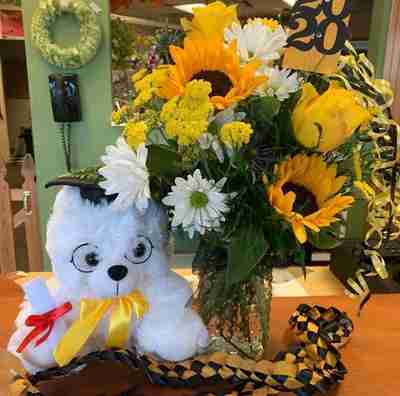A white graduation bear sitting next to a bouquet of dandelions in a vase