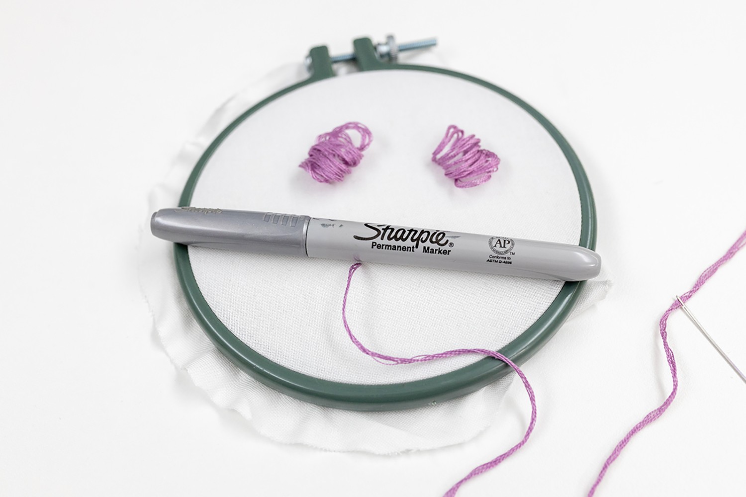 A pen lies on the hoop, with satin stitch tunnels behind.