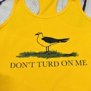 Picture of a gold and yellow women's tank top with a picture of a seagull standing in the grass. Text on the women's tank top says "Don't Turd On Me." Similar to the Gadsden "Dont Tread On Me" Flag
