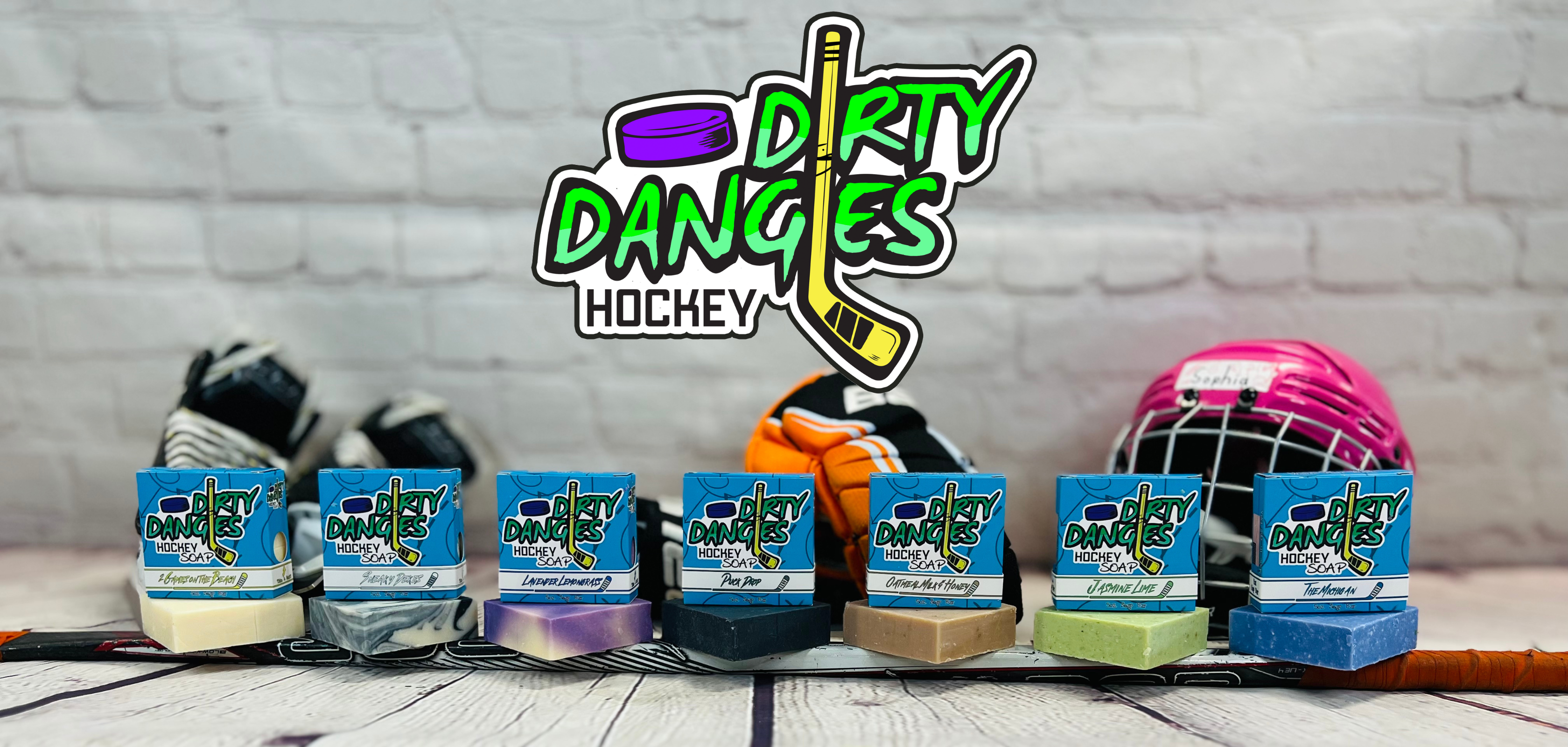 7 dirty dangles hockey soap bars sit on a hockey stick with hockey equipment in the background.