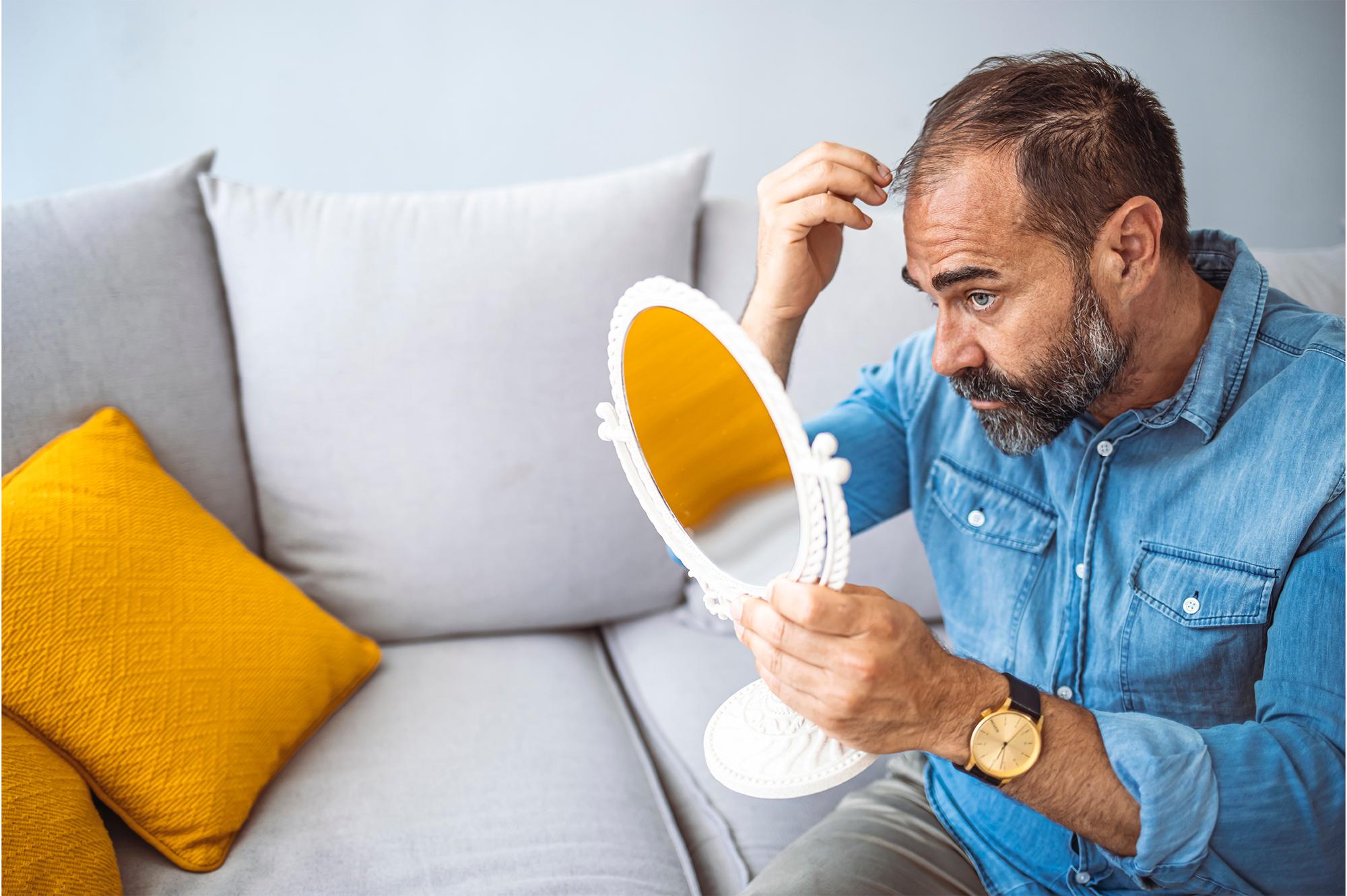 Man checking his hair in the mirror with a frustrated expression after using a hair growth shampoo that failed to meet expectations.