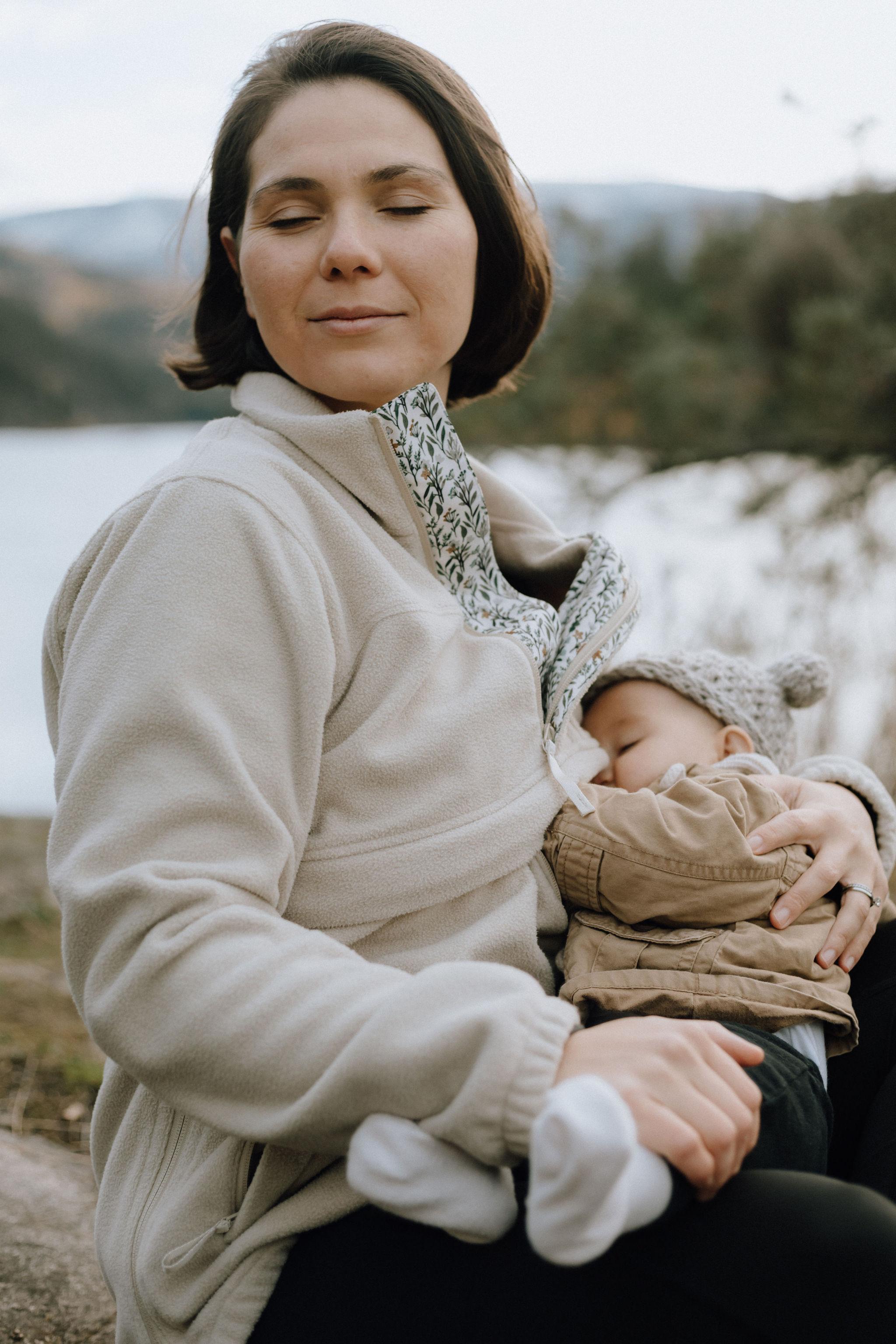 Mom nursing her baby in the forest while wearing her All Phases Fleece
