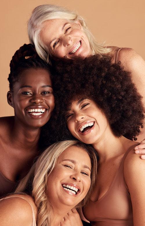 Group of four diverse women of different ages and skin tones laughing and embracing, radiating joy and confidence.