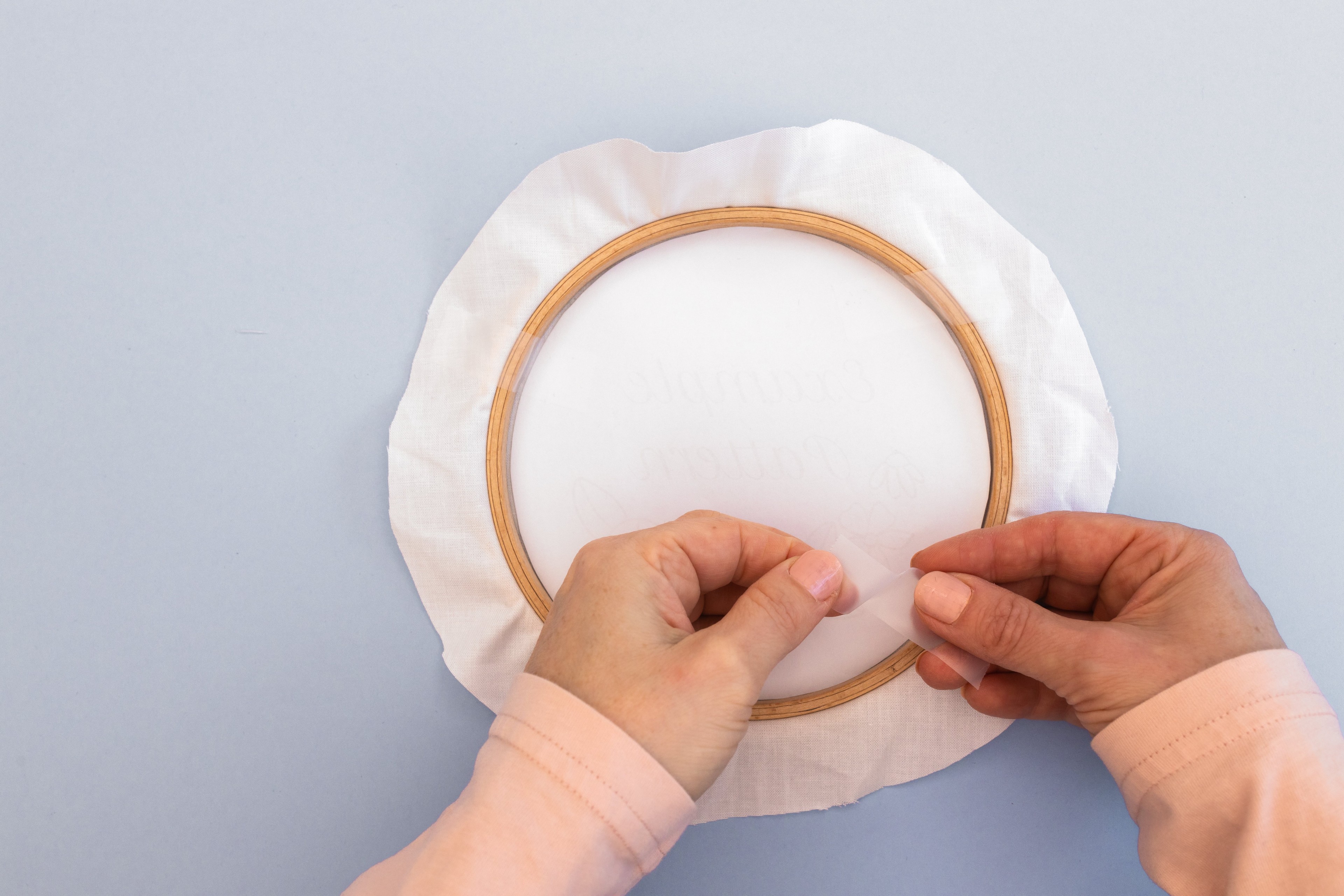 A hand holds a cellotape in front of the dressed hoop.