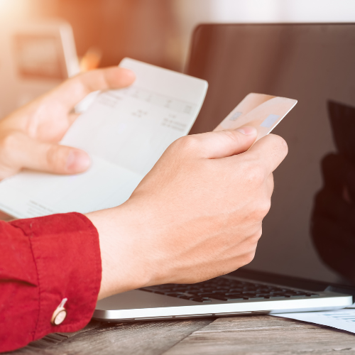 Hand holding credit card in front of laptop calculating the ongoing fees to expect