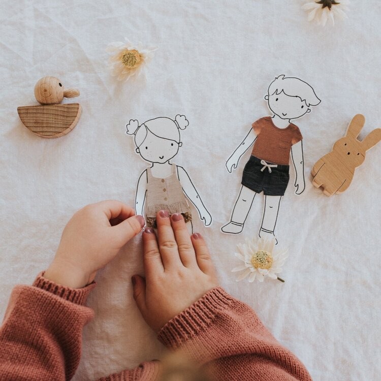 A little girl puts shorts on the paper doll.