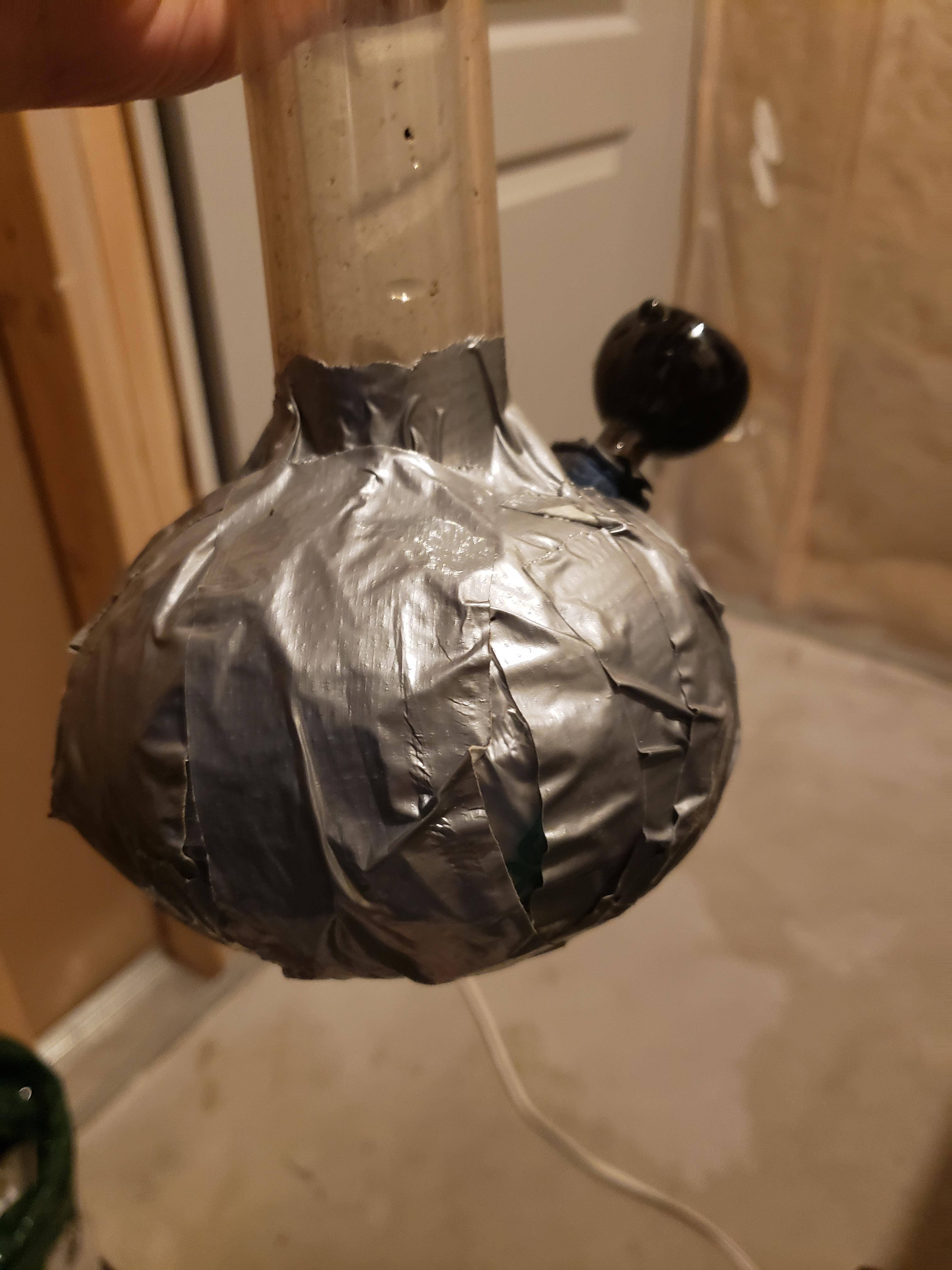 An extreme example of the "Hazardous Hunch": a round based beaker bong completely covered in an entire roll of duct tape, obscuring all the glass. This image warns against the dangerous and structurally unsound practice of using household adhesives for pipe repair, which can release toxic fumes and chemicals when heated.