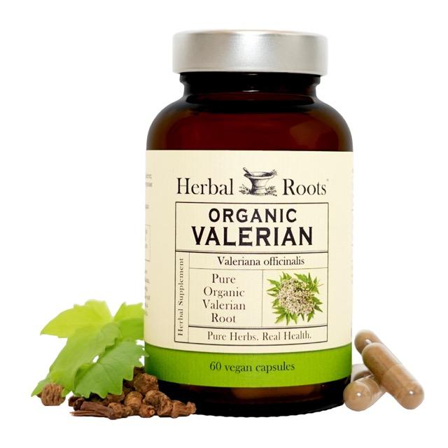 Bottle of Herbal Roots Organic Valerian supplement with valerian root and leaves to left of bottle and capsules to right of bottle, with white background