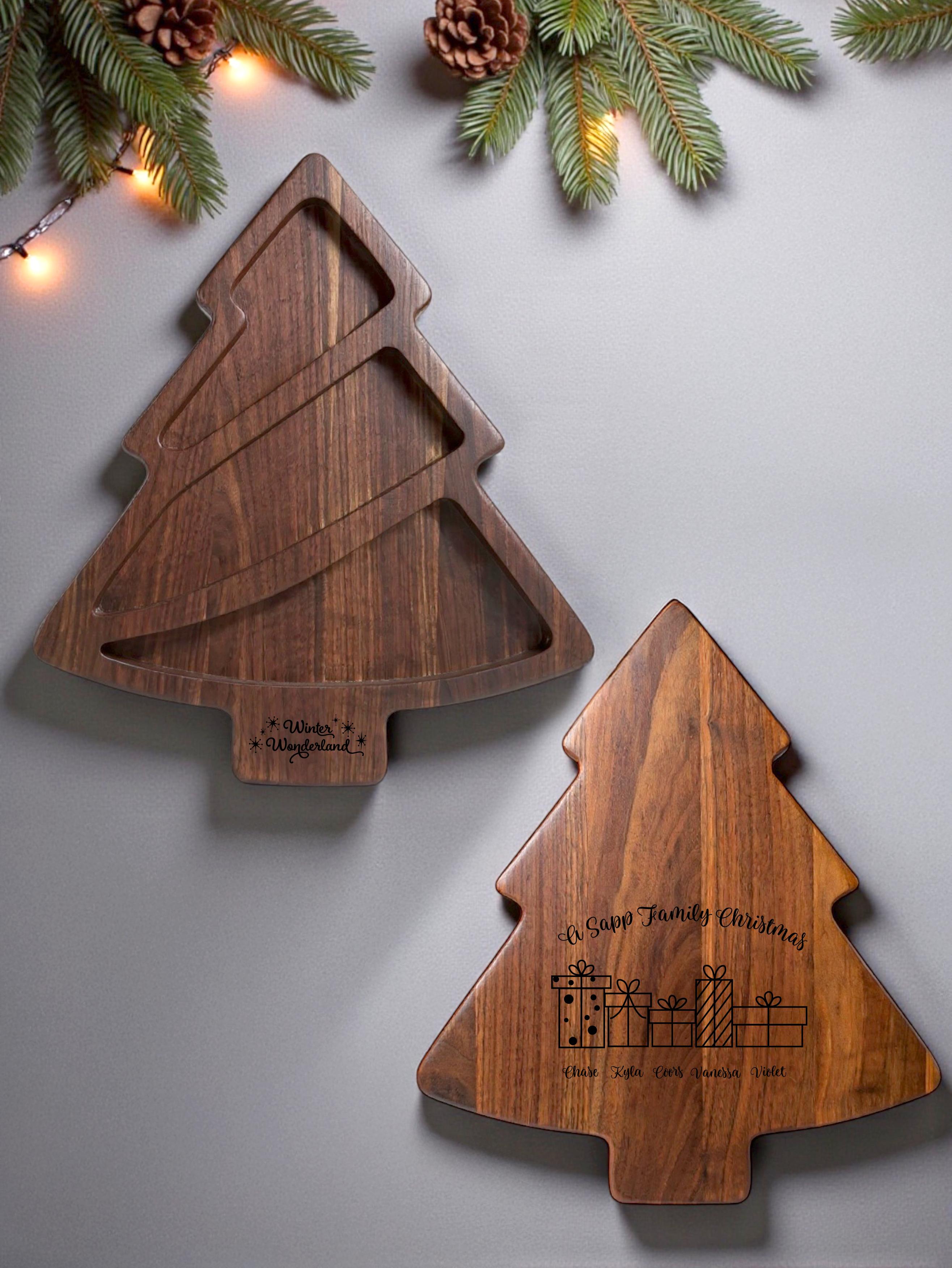 Walnut holiday charcuterie boards shaped like Christmas trees, one with serving compartments and one with a personalized engraved design, styled on a light background with festive pine branches and warm lights.