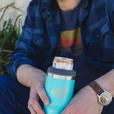 A man holding a blue dirty dangles 2 in 1 drink tumbler can cooler outside.