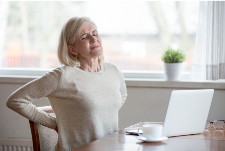 Older woman clutching lower back in pain sitting at her computer