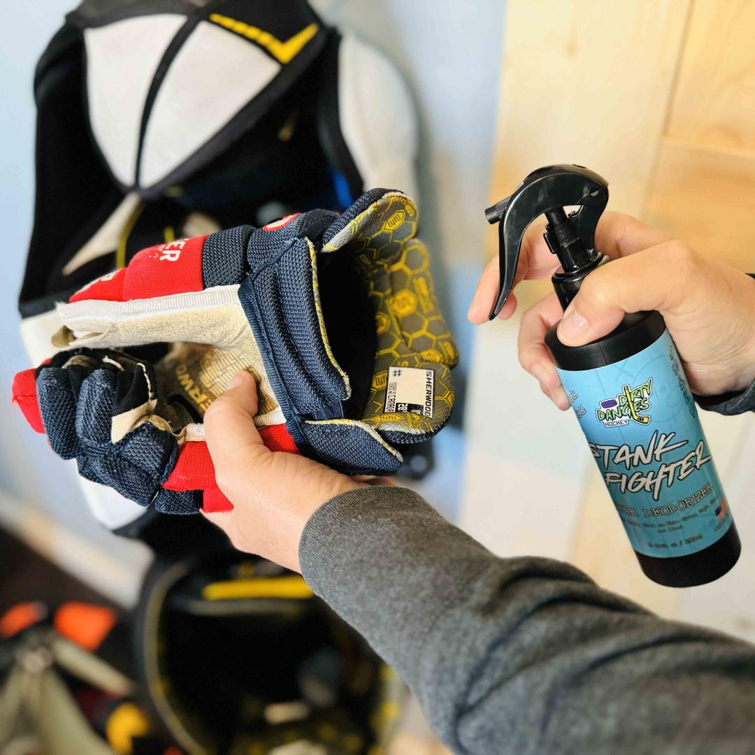 A woman spraying Stank Fighter Hear deodorizer onto a red and blue hockey glove