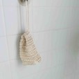 a tan sisal soap bag hangs in a shower