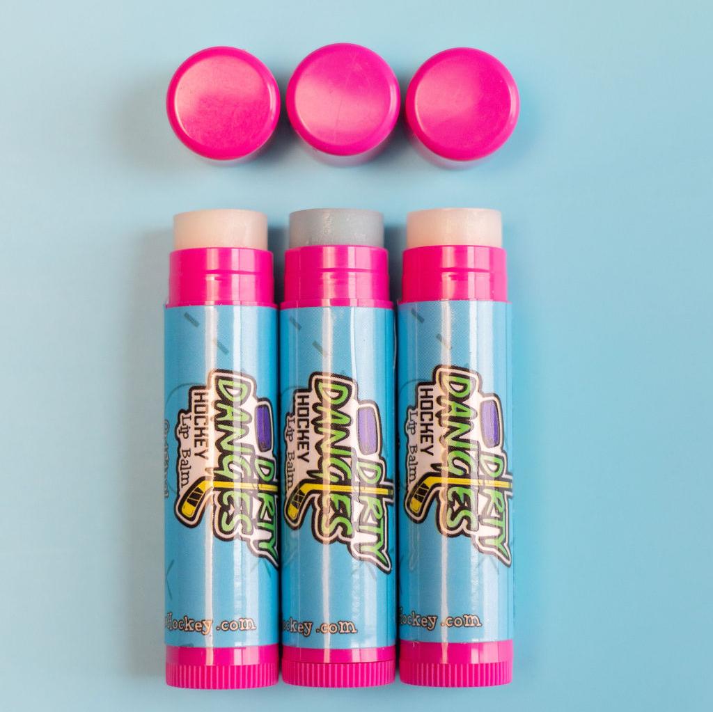 3 pink and blue sticks of lip balm on a blue background. Dirty Dangles hockey lip balm