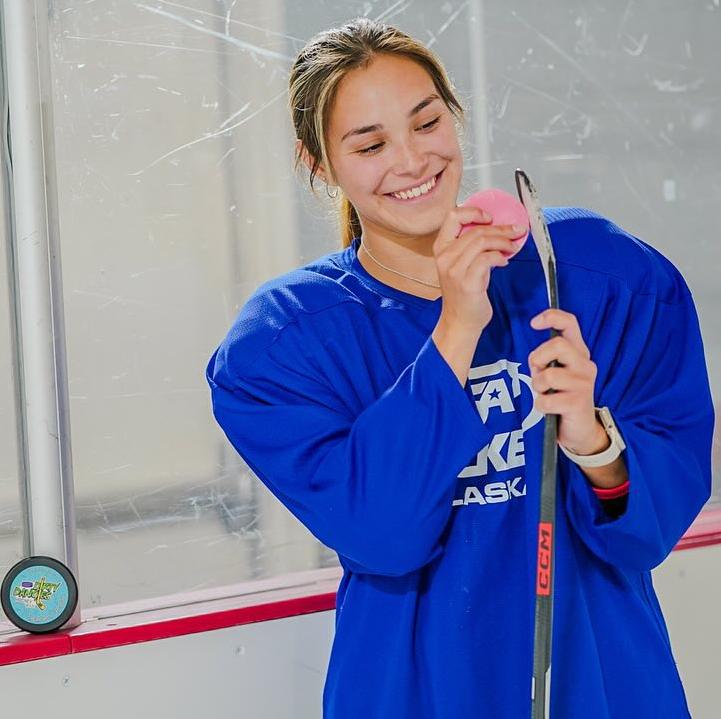 Girls hockey player applying Dirty Dangles hockey stick wax to her stick at the rink.