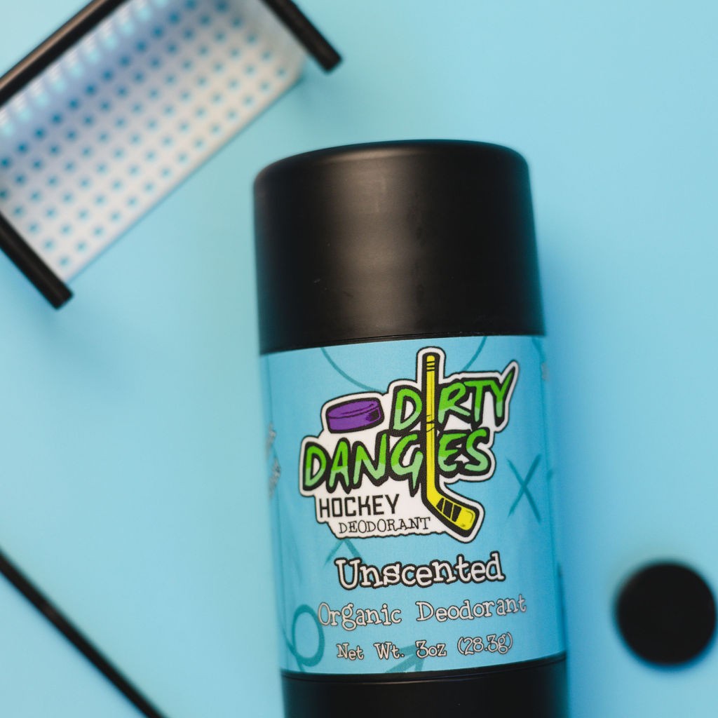 A tube of dirty dangles natural probiotic deodorant on a blue background with hockey toys