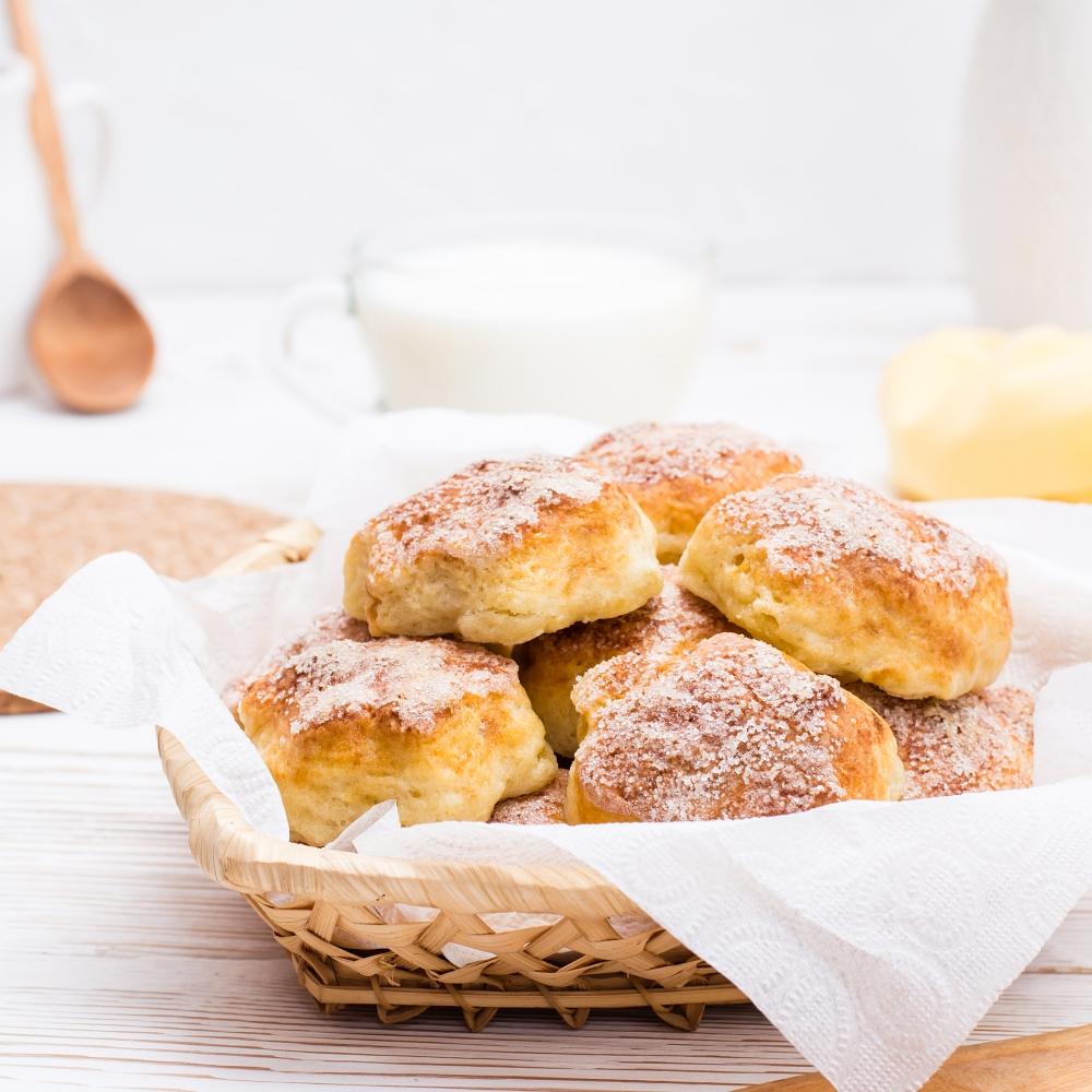 Cottage cheese cookies sprinkled with sugar in a basket and a cup of milk on a wooden table