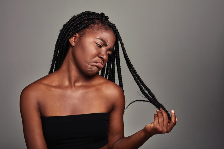 black woman sad, looking at her braids