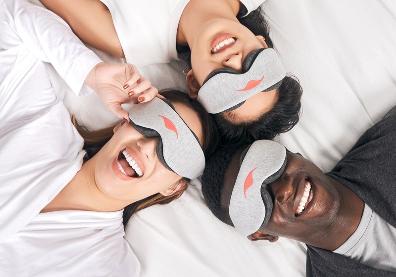 Two women and a man wearing sleep masks to achieve complete darkness for the best sleeping environment.
