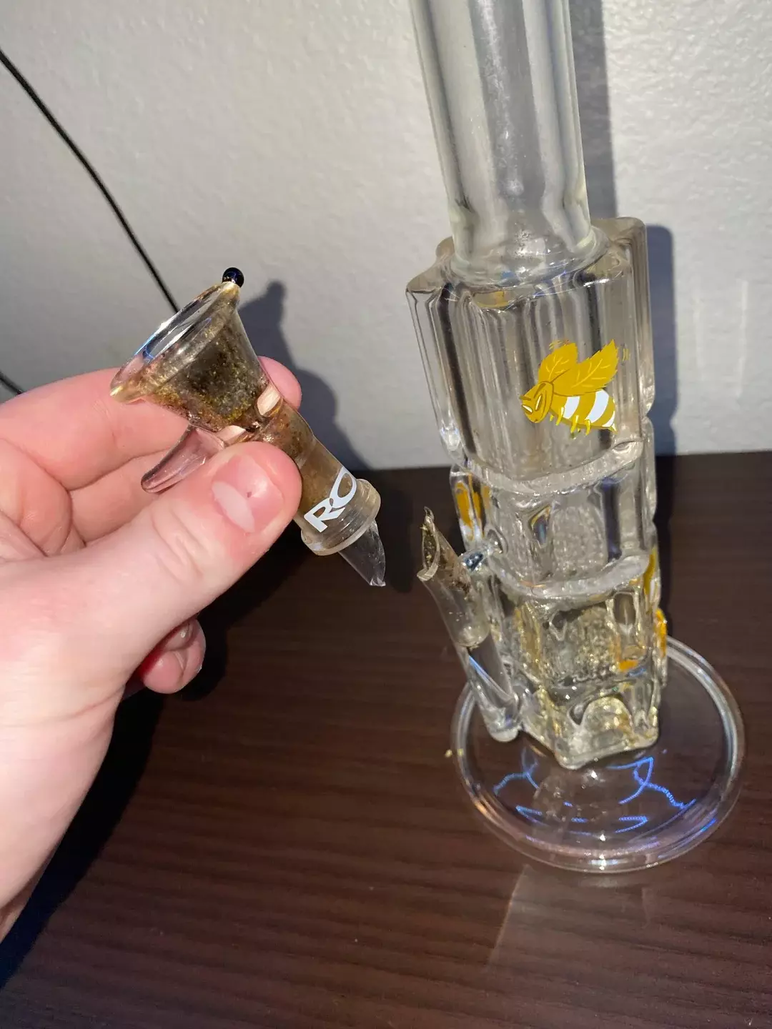 A broken dab rig showing the male joint snapped off the main body. A hand is dangerously holding the broken joint in place, illustrating the hazardous and unsafe practice of attempting to use a structurally compromised pipe instead of properly retiring the damaged piece.