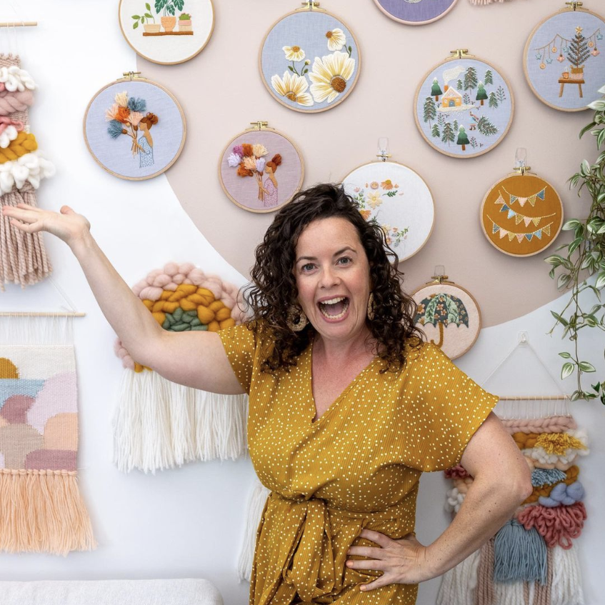 This is an image of Julie (Clever Poppy) pointing to all the embroidery patterns she has created.