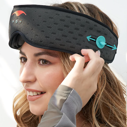 A girl wearing a sleep mask with headphones pointing to the adjustable tab of the built-in speaker.