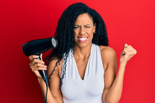 Black woman with natural hair holding blow dryer frustrated about heat damage