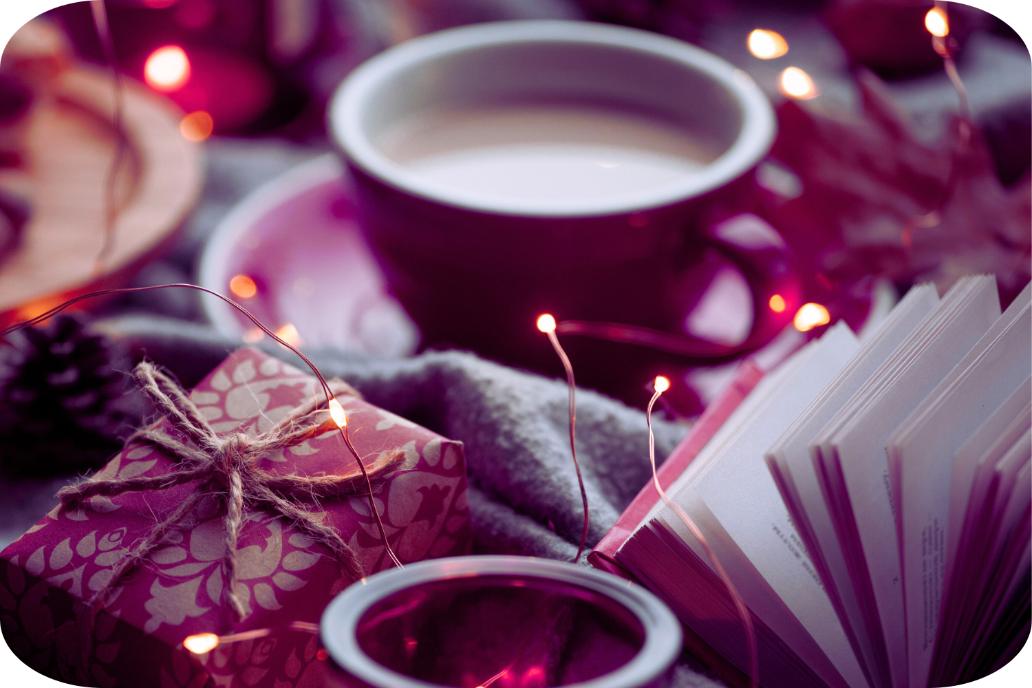 red mug, candle, decorative lights, and an open book