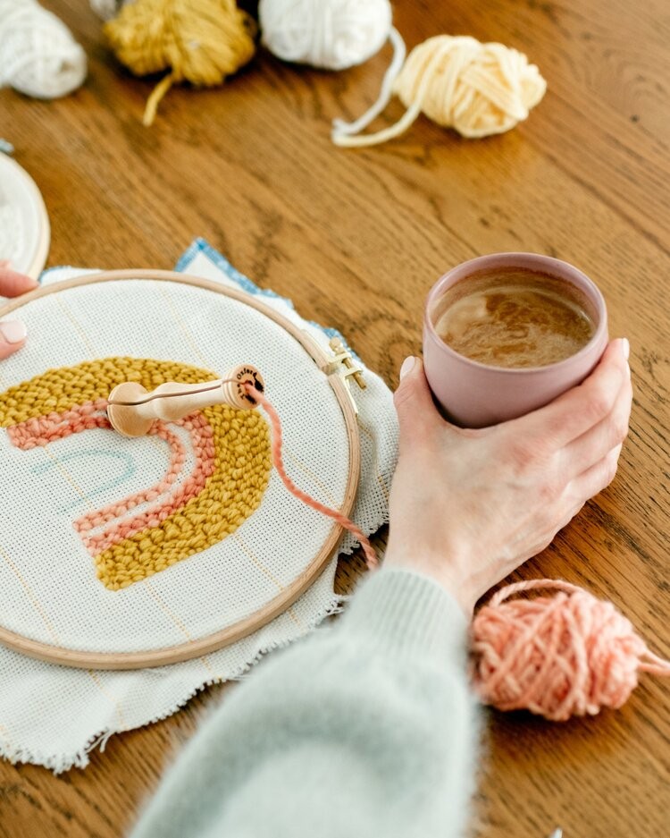 Someone enjoys a cup of coffee with their punch needle project.