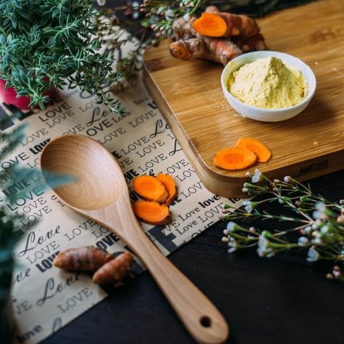 wood spoon and cutting board with green herbs and turmeric
