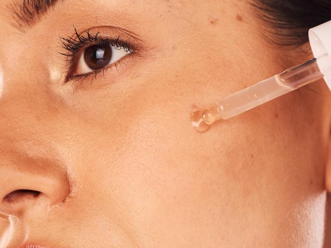 Woman applying skincare serum as the second step in her skincare routine.