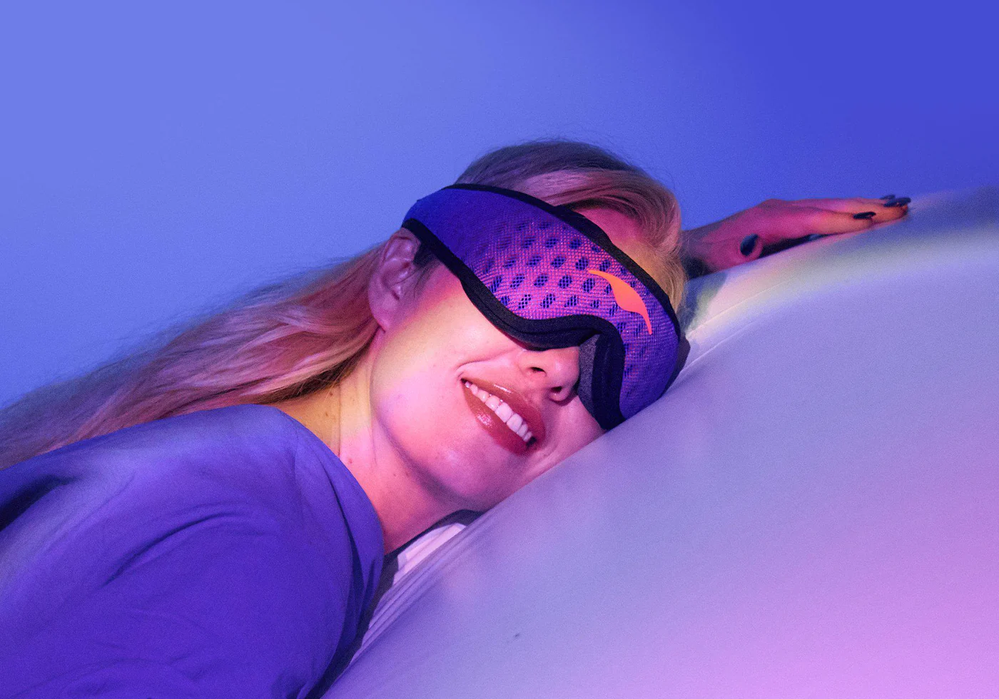A blonde girl napping after eating wearing a blue mesh sleep mask for side sleepers.