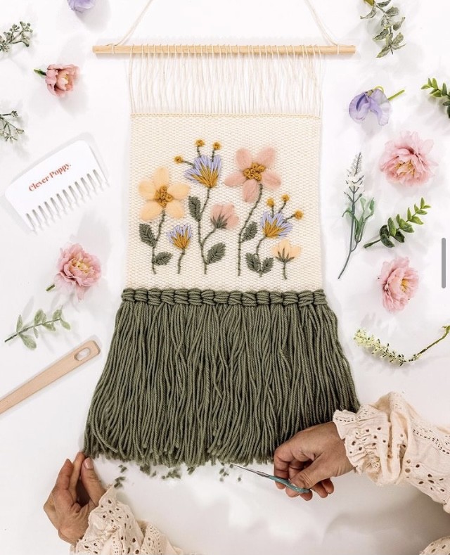 The weaving 'A Woven Meadow,' lies on a table being trimmed by hands.