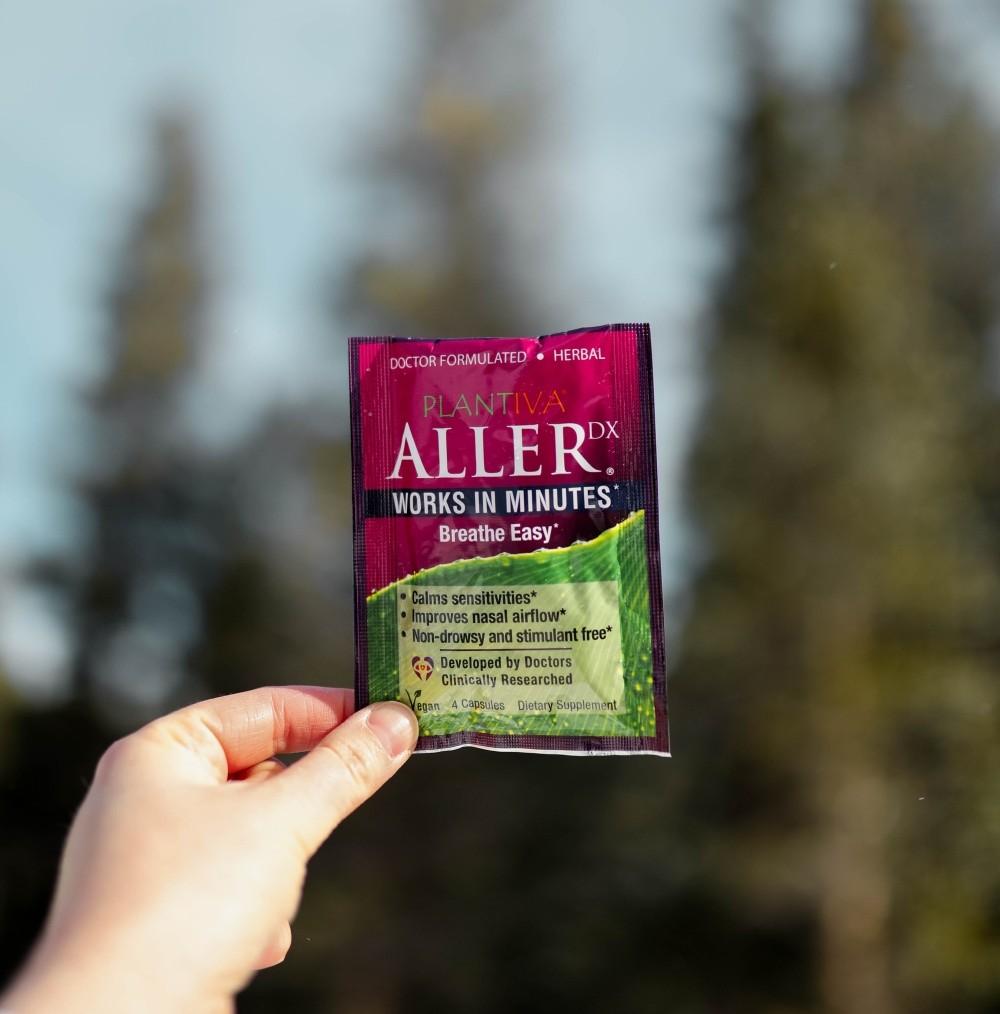 A packet of AllerDx is held up against a backdrop of evergreen trees