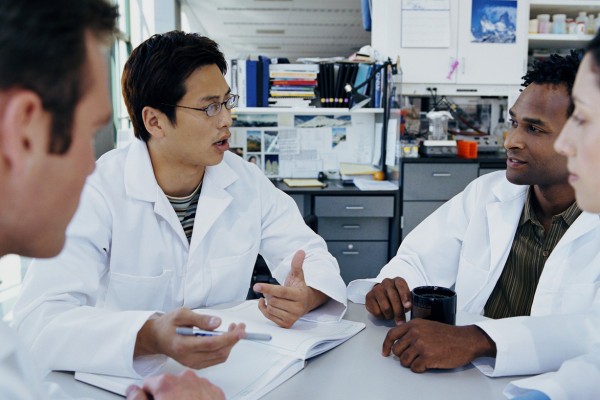 group of university students wearing lab coats, sitting at a table and discussing a topic