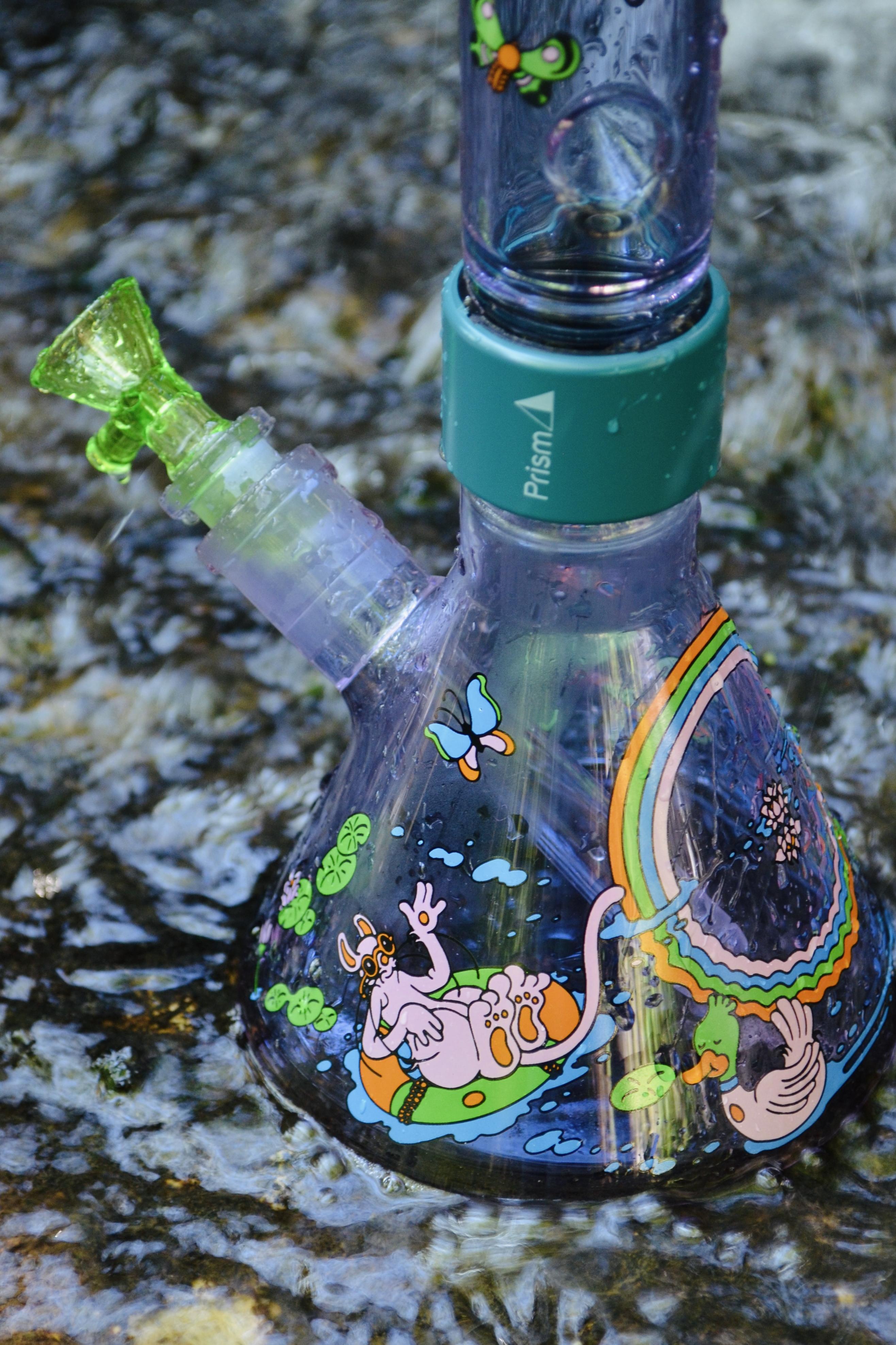 An image of Prism purple glass beaker bong in the water of a creek and the glass has POnd Life decal on it