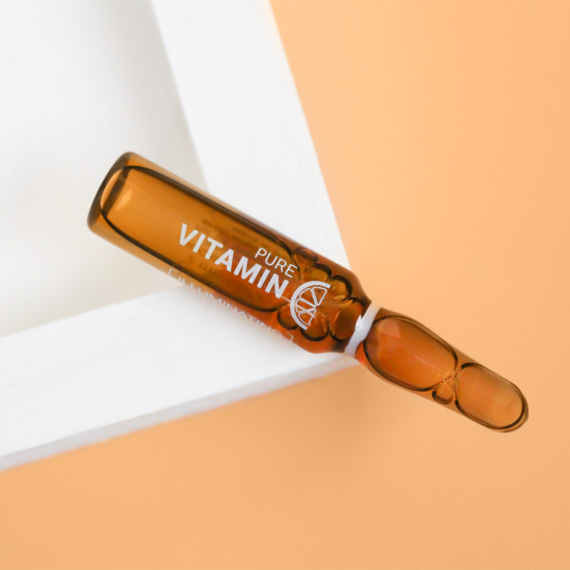 Vitamin C Ampoule laying on a white corner on top of an orange background