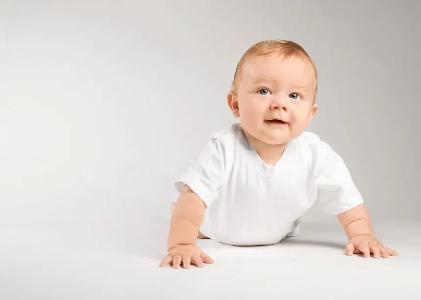 A baby crawling on the floor, surrounded by colorful baby clothes scattered nearby
