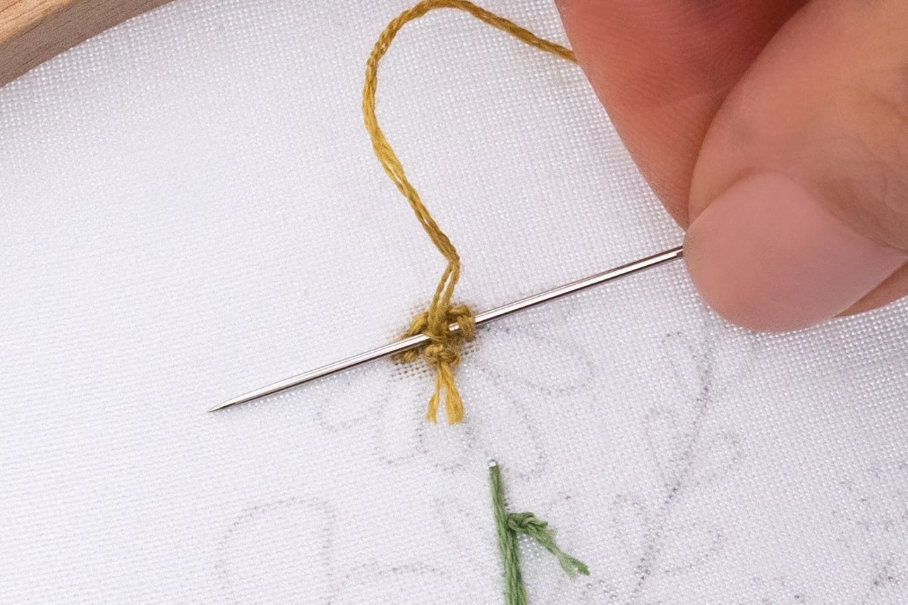 A needle is being pulled through the back of a french knot.