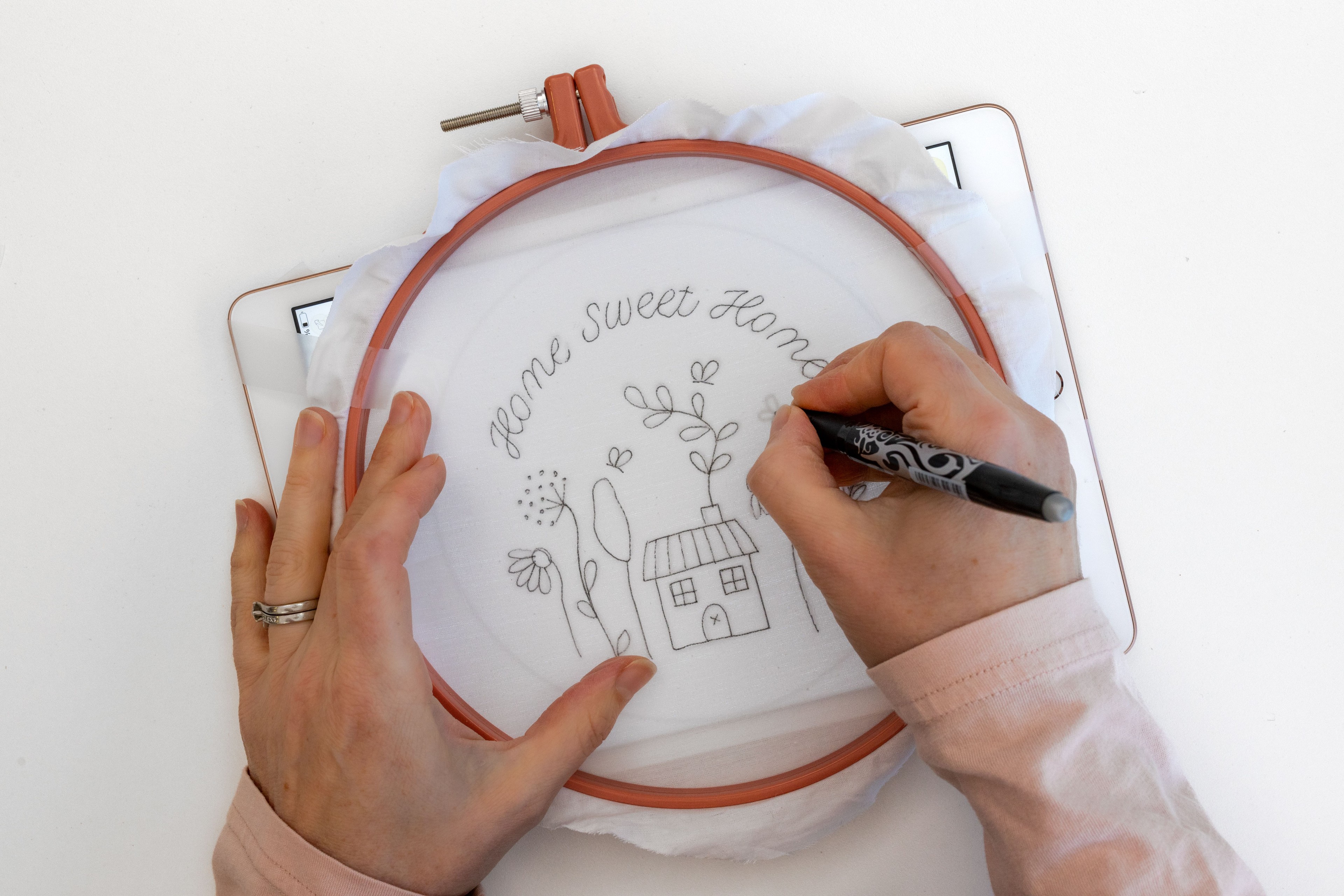A hand draws a pattern on a hoop using a tablet as a light source.