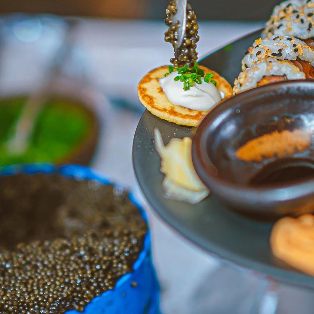 Putting a spoonful of caviar over blini with crème fraîche and fresh chives