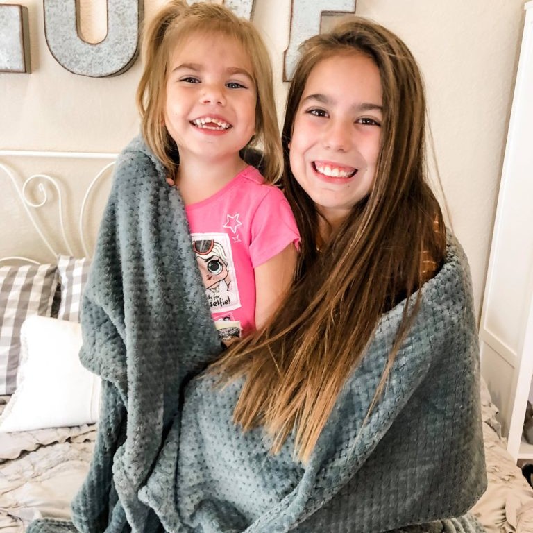 two sisters smiling wrapped in a gray blanket