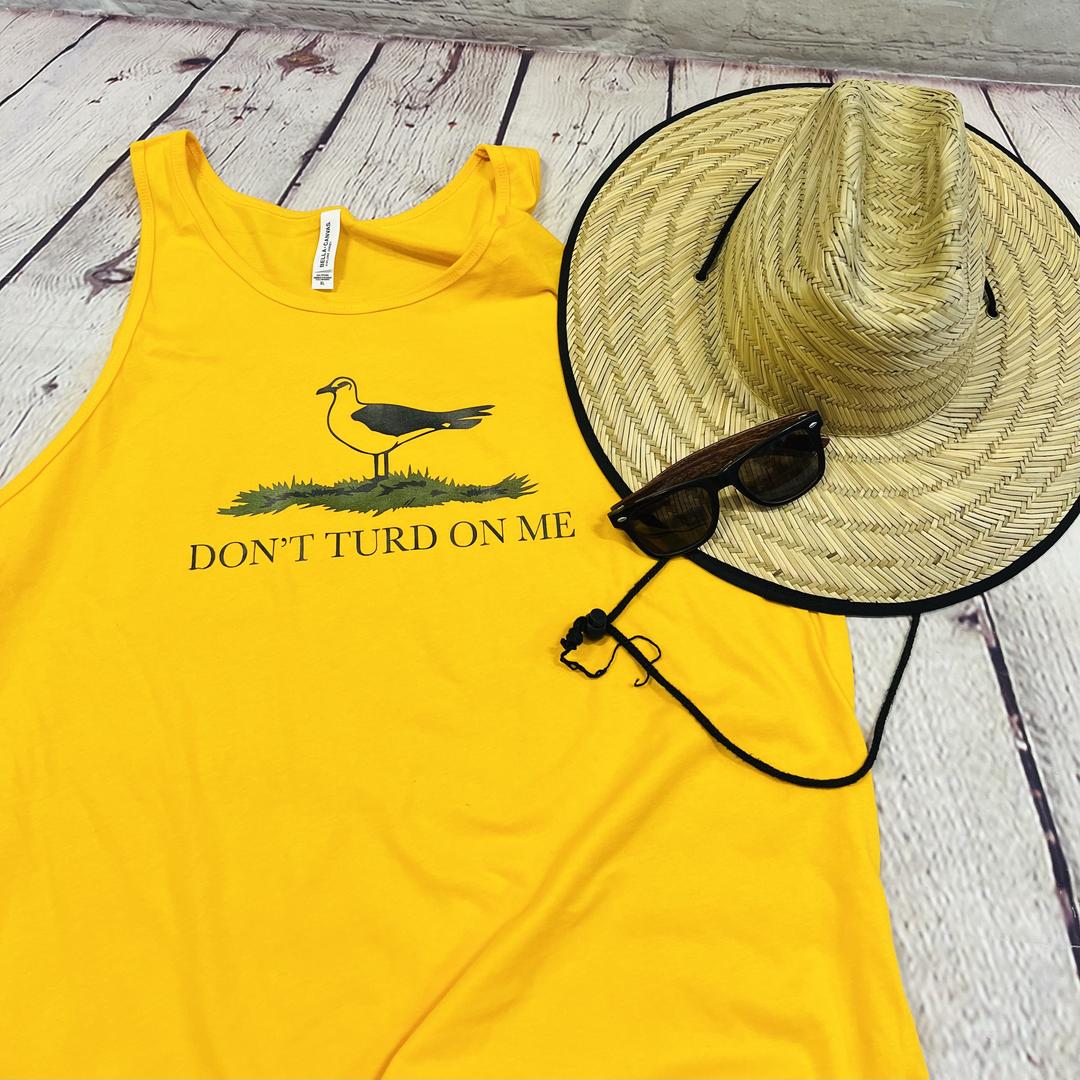 Picture of a gold and yellow men's tank top with a picture of a seagull standing in the grass. Text on the men's tank top says "Don't Turd On Me." Similar to the Gadsden "Dont Tread On Me" Flag