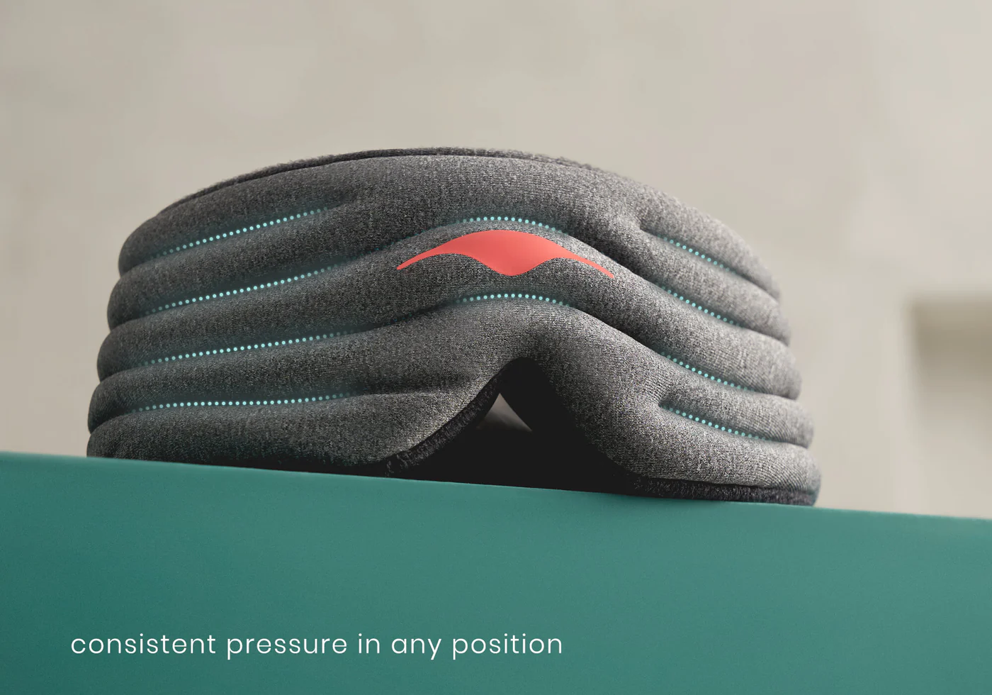A gray pressure eye mask with aqua stitching on top of a green surface.