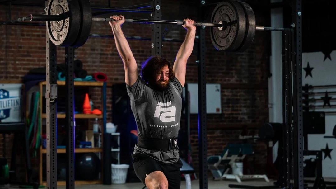 Woman lunging while lifting a dumbbell above her head wearing black lever belt