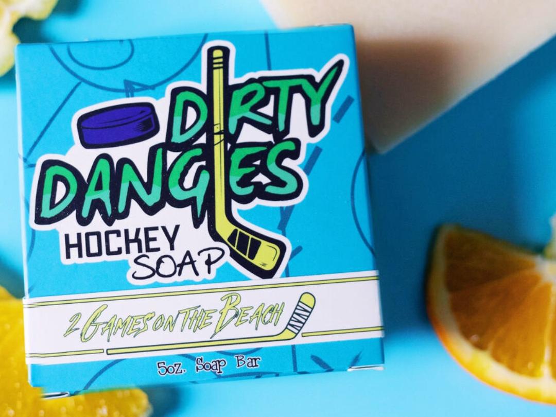 A yellow 2 games on the beach hockey soap bar on a blue background with a blue box, lemons and lavender