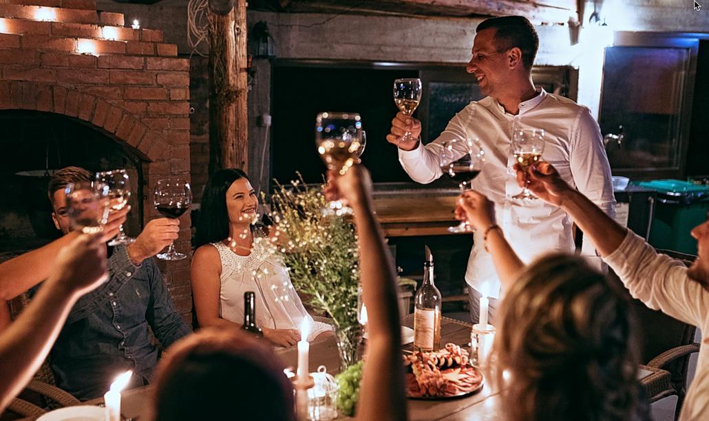 dinner party participants cheering the host with glasses of wine. Its a warm inviting picture. representing how to host a dinner party.